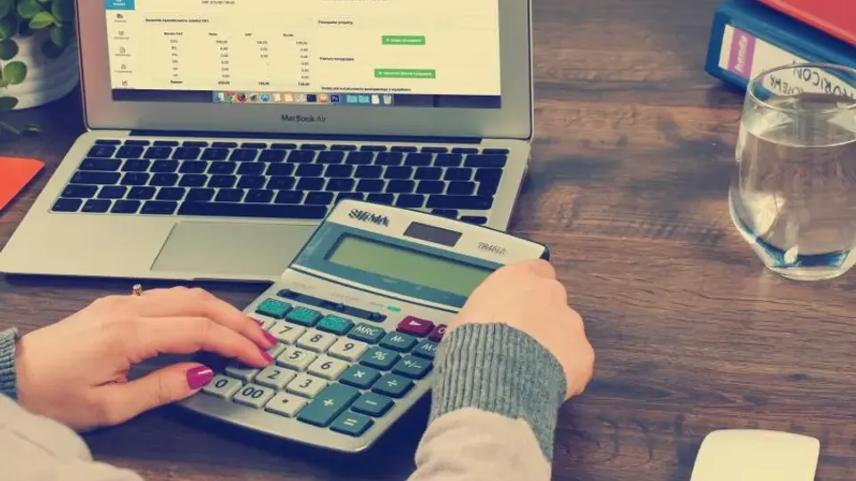 Person working with a calculator and spreadsheets on a laptop